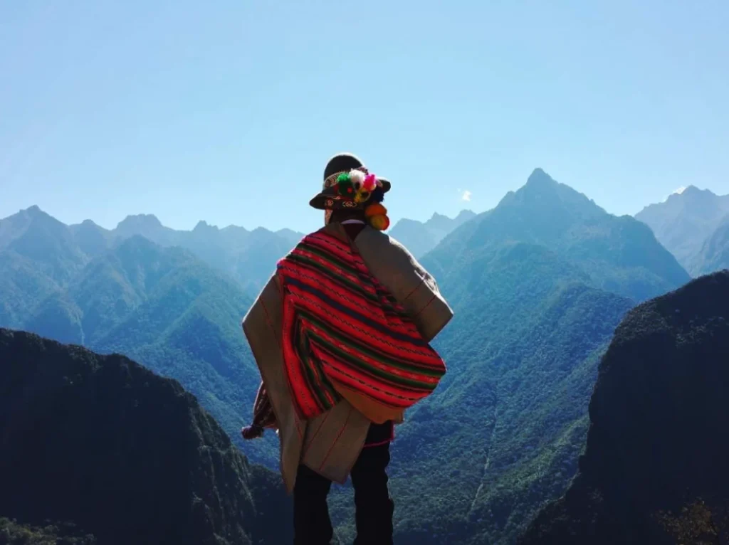 Man op de rug met poncho en traditionele hoed kijkt naar de bergen van de Andes.