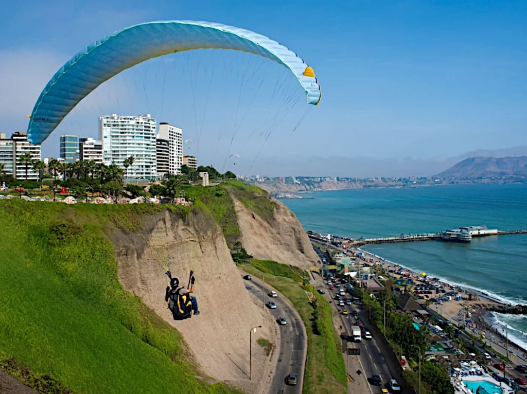 Paraglider boven de kliffen van de Malecón in Miraflores, Lima, met de kustweg en de oceaan eronder.